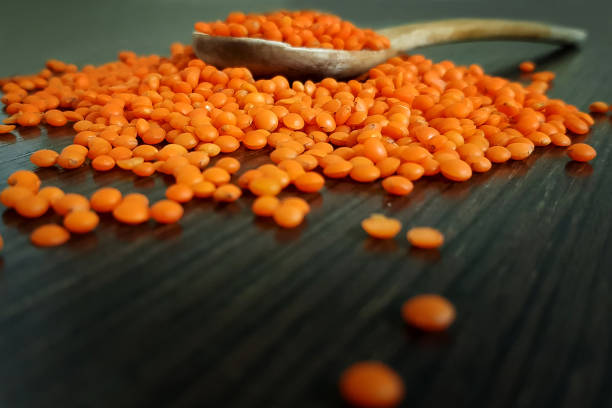 Orange lentils in veneer. On a wooden dark background I am sprayed in a spoon
