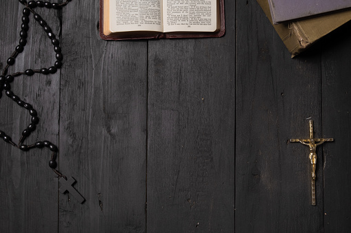 Flat lay image of New Testament, cross and rosary on old black background