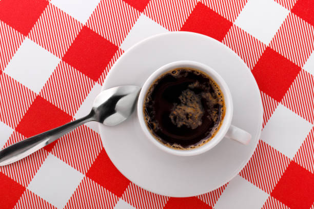 istock Cup of coffee on white and red checkered tablecloth. Top view 1127635773