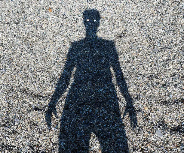 Shadow of faceless man on a rocky sand beach