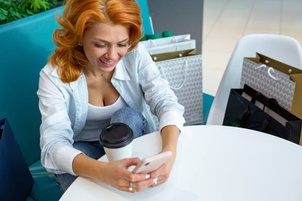 istock Woman using mobile phone while drinking coffee in cafe at shopping mall 1127639280