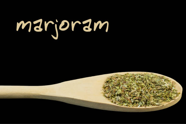 istock marjoram on wooden spoon isolated on black background 1127639555