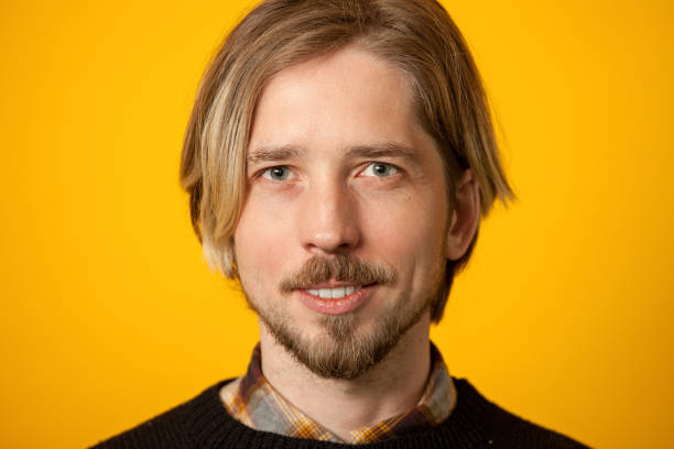 Studio portrait of a 30 year old bearded man in a black sweater on a yellow background