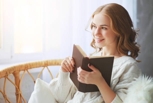 istock happy young woman reading a book by window 1127641072