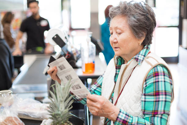 prudent senior woman looking at her coupons before paying for her groceries. - cheep imagens e fotografias de stock