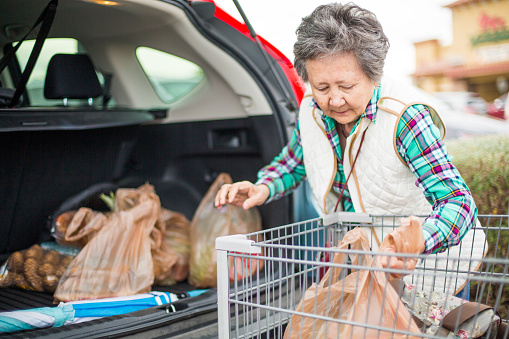 Senior woman loading grocery bags in the trunk of her car.