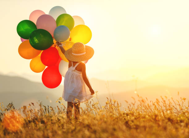 . счастливый ребенок с воздушными шарами на закате летом - sun sky child balloon стоковые фото и изображения