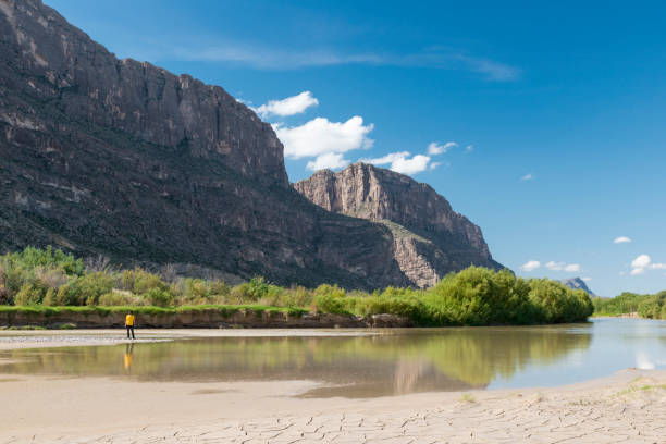 Man with a had looking to the side at a dry riverbed. Santa Helena canyon of Big Bend park on the background.