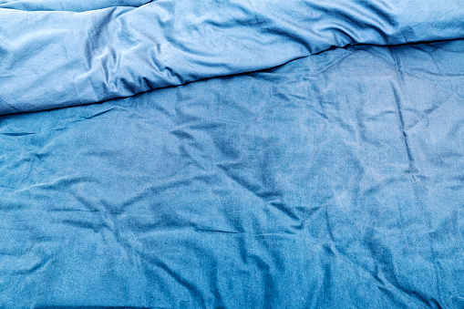 Abstract close-up of a messy, wrinkled, kinda grubby and well-used blue bed sheet with matching blue duvet - pulled back at top of frame. A few pet hairs and quite a lot of lint and dust spots here and there. Potential backgrounds.