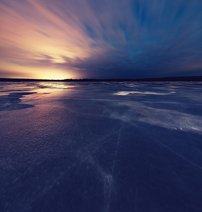 The bright lights of a nearby airport illuminate clouds above a frozen lake.  Long exposure.