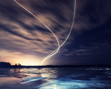 Two passenger jets take off from an airport above a frozen lake.  Long exposure.