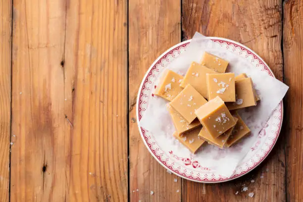 Photo of Fresh caramel fudge candies on a plate. Wooden background. Top view. Copy space.