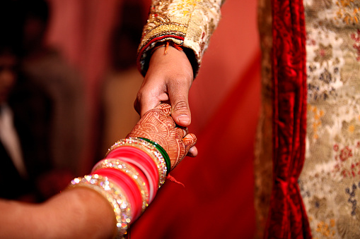 Indian groom holding bridal hand whe she coming on the stage. Weddings in India vary regionally, the religion and per personal preferences of the bride and groom. They are festive occasions in India, and in most cases celebrated with extensive decorations, colors, music, dance, costumes and rituals that depend on the religion of the bride and the groom, as well as their preferences.