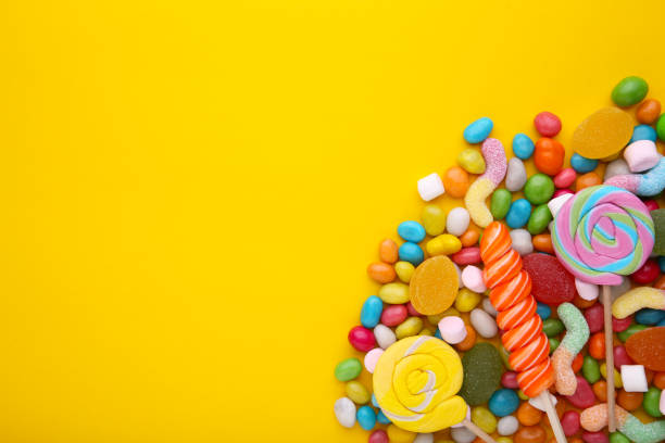 istock Colorful lollipops and different colored round candy on yellow background 1127706572