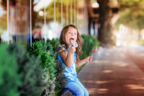 mała dziewczynka smakuje cukierkami na patyku - people eating walking fun zdjęcia i obrazy z banku zdjęć