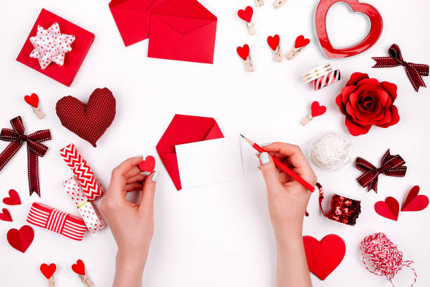 istock Women's hands holding valentine card on white background with romantic decoration. flat lay 1127710820