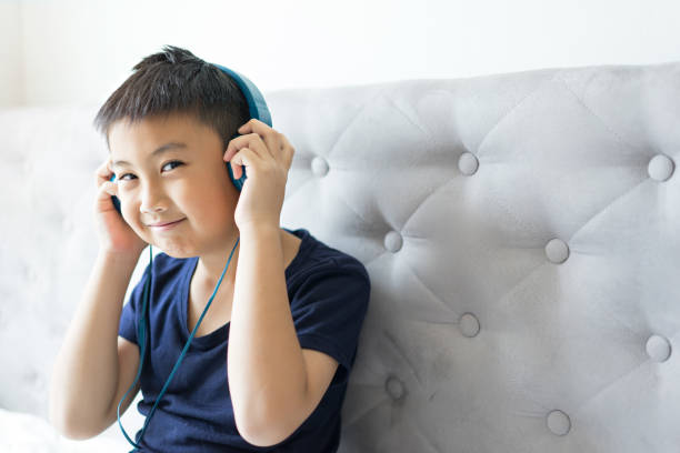 リラックスのための寝室のベッドで音楽を聞いて幸せの小さな男の子 - chinese ethnicity audio ストックフォトと画像