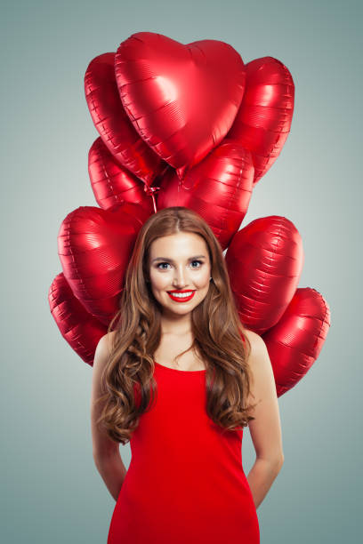Girl with heart balloons. Woman with red lips makeup wearing in red dress. Valentines people and Valentine's day concept Girl with heart balloons. Woman with red lips makeup wearing in red dress. Valentines people and Valentine's day concept valentine s day holiday stock pictures, royalty-free photos & images