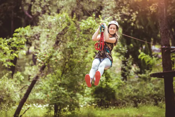 Happy school girl enjoying activity in a climbing adventure park on a summer day