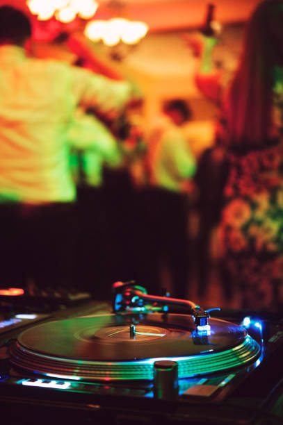 A vinyl turntable with Dj hands with people dancing in the background at a wedding event in California USA