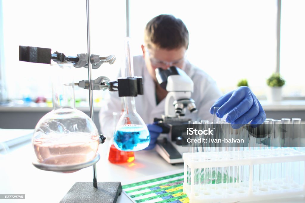 Portrait of a young chemist looking in binocular Portrait of a young chemist looking in binocular microscope looking for pathology analyzes patient at medical hospital for treatment disease tumors Pharmacy Stock Photo