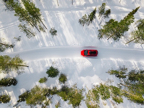 Aerial view of red car driving through the white snow winter forest on country road in Finland, Lapland.