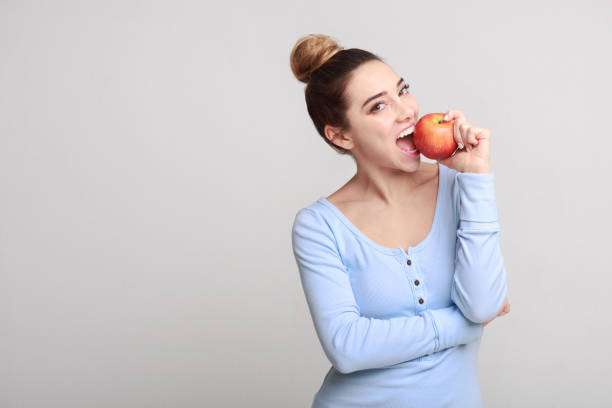 Healthy eating. Pretty girl biting fresh apple Healthy eating. Pretty girl biting fresh apple over grey background, copy space 1 APPLE stock pictures, royalty-free photos & images