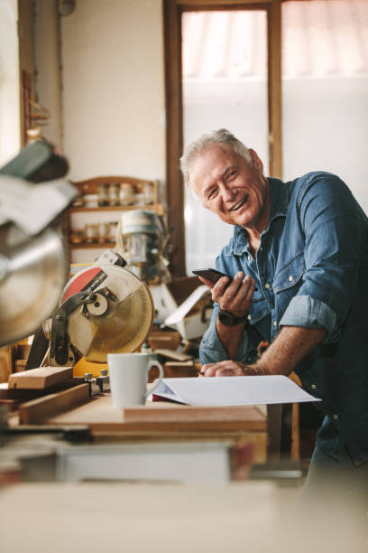 istock Happy senior male carpenter with phone in workshop 1127734334