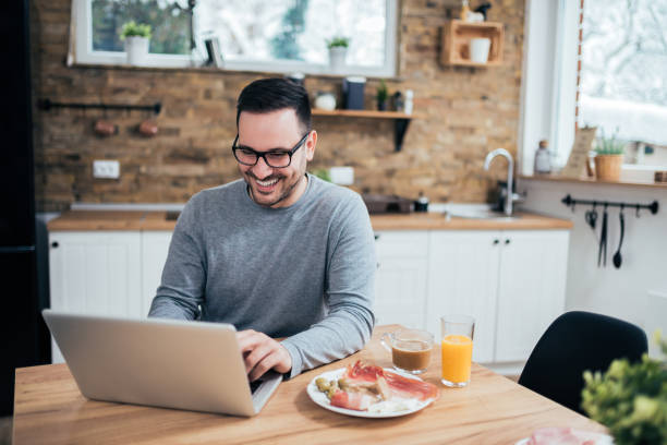 istock Happy handsome man using laptop in the morning at the kitchen table. 1127738473