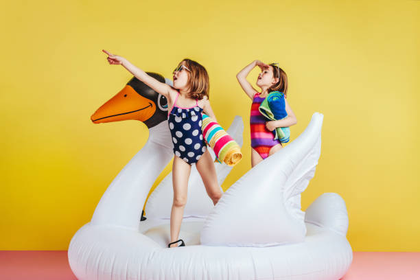 сестры-близнецы в купальниках на надувном фламинго, смотря в сторону - water toy стоковые фото и изображения