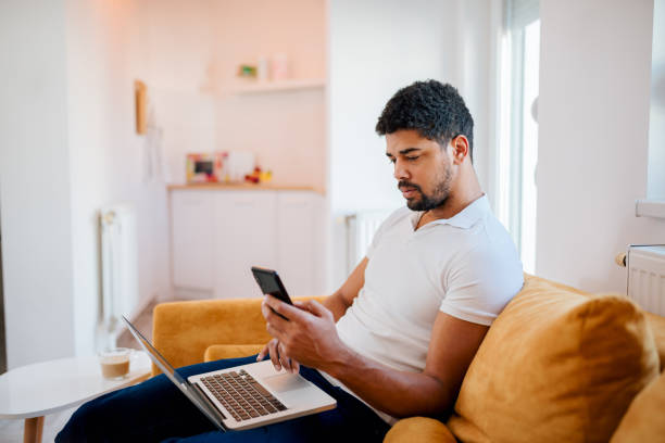 istock Working from home. Young man sitting on sofa with laptop and mobile phone. 1127739617