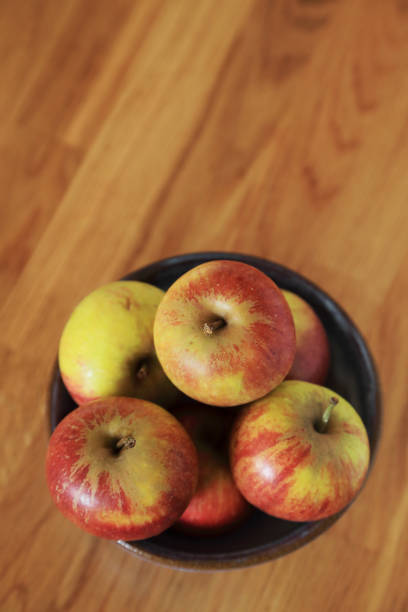 Composition with Yellow Red Apples in ceramic bowl top view vertical on wooden background.
