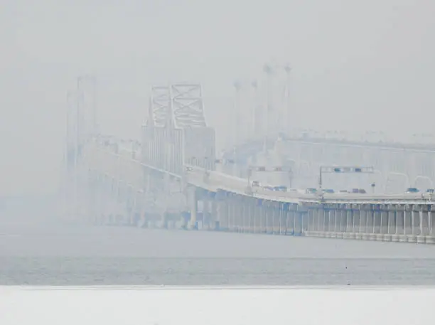 Photo of Chesapeake Bay Bridge on a gloomy, foggy winter day with ice on the bay in the foreground.