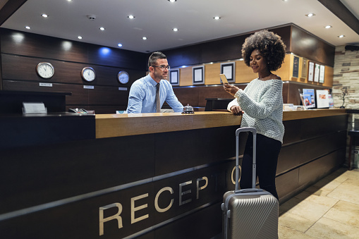 Pretty young African-American woman texting on her phone while checking in at the hotel