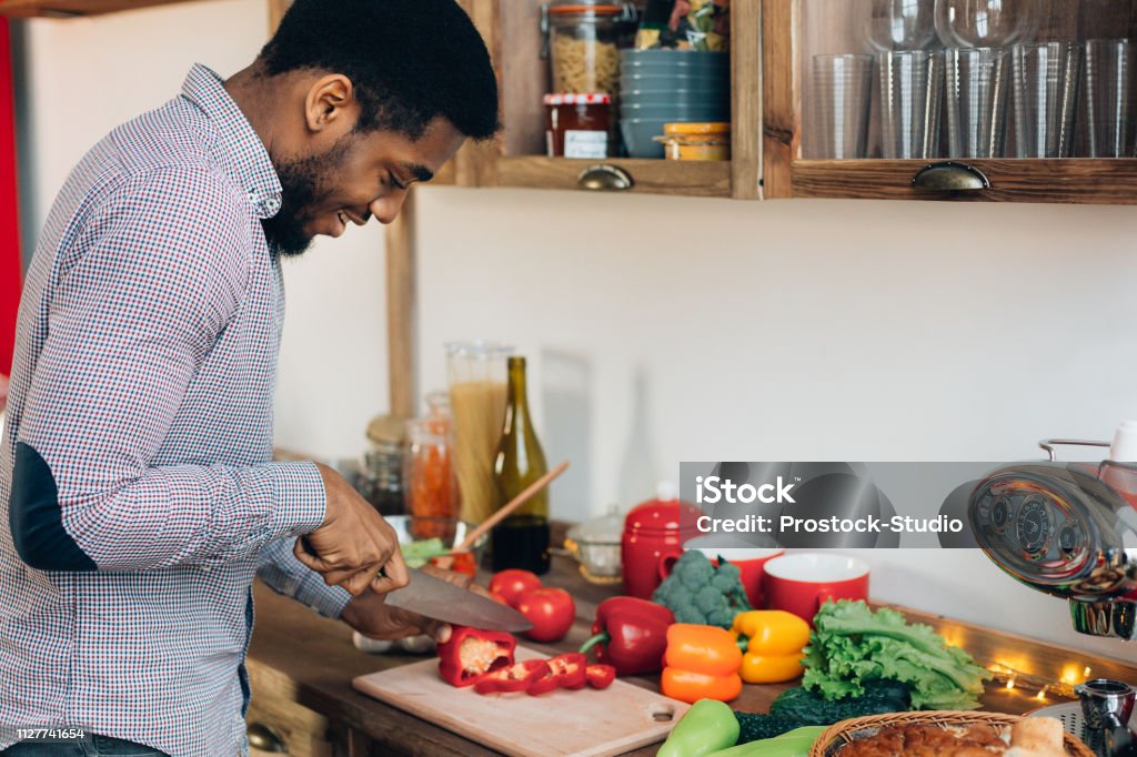 African-american man cutting bell pepper in kitchen African-american man preparing delicious and healthy food in kitchen, cutting fresh vegetables, copy space Cooking Stock Photo