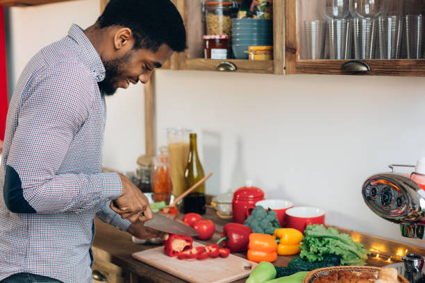 african-american man cutting bell pepper in kitchen - vegetable men cutting adult imagens e fotografias de stock