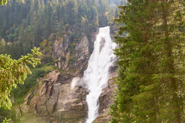 Atmospheric minimal landscape with vertical big waterfall on rock mountain wall. Powerful large waterfall in dark gorge. Nature background of high vertical turbulent falling water stream on wet rocks.