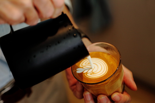 Barista using pitcher for pouring froth milk to cup of coffee latte with tulip pattern on top