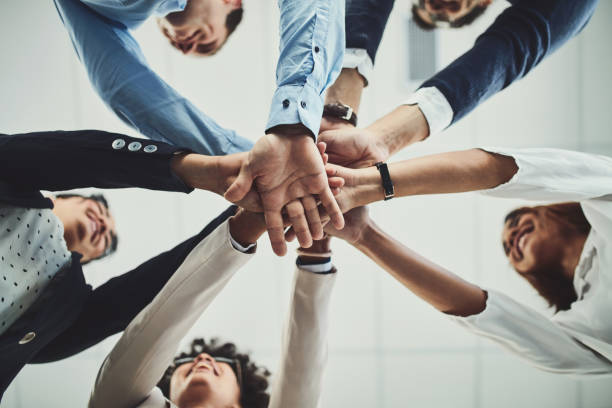Here we go guys! Low angle shot of a group of businesspeople forming a huddle with their hands inside of the office during the day sea of hands stock pictures, royalty-free photos & images