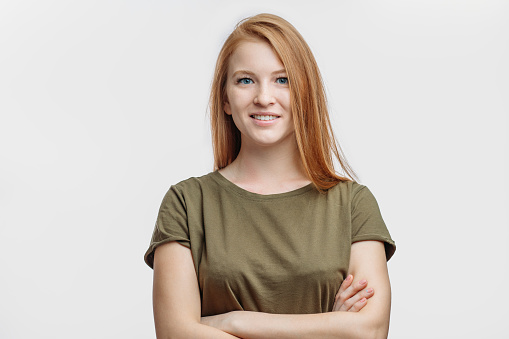 a happy pretty young lady with red hair standing with arms crossed. people concept