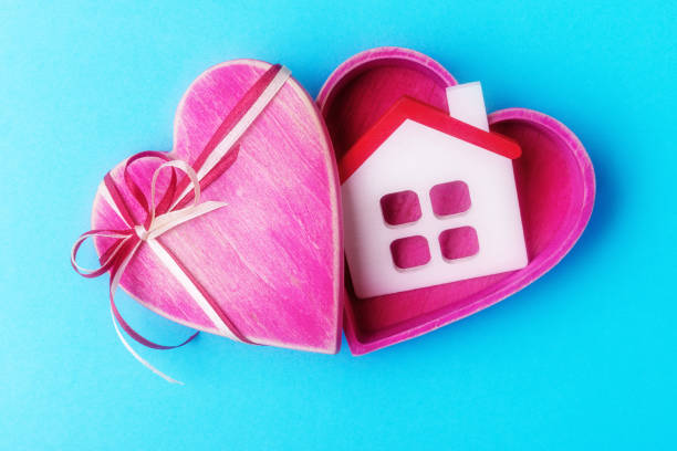 istock Heart shaped gift box with house model on blue background 1127756487