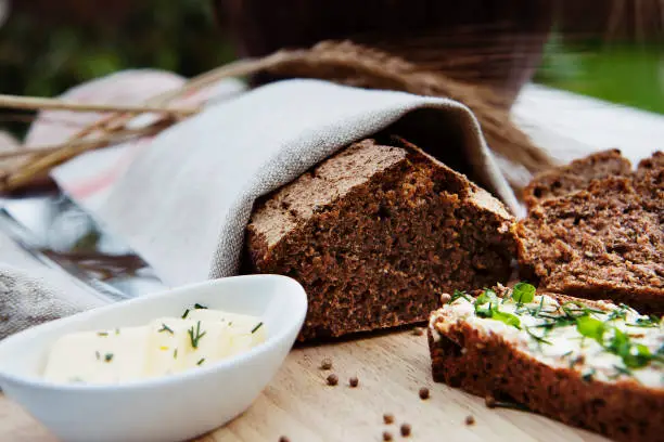Vilnius, Lithuania - September 23, 2011: tasty looking fresh homemade rye bread sliced in tow pieces, covered with natural linen kitchen towel and served on a wooden cutting boar on a table outdoors.