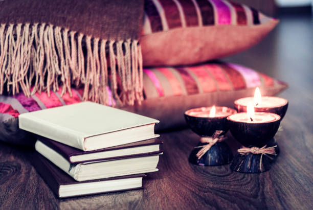 Stack of books and burning candle are on the night stand on the foreground. The bed is in the background