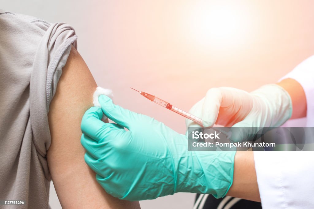 Vaccination healthcare concept. Hands of doctor or nurse in medical gloves injecting a shot of vaccine to a man patient Injecting Stock Photo