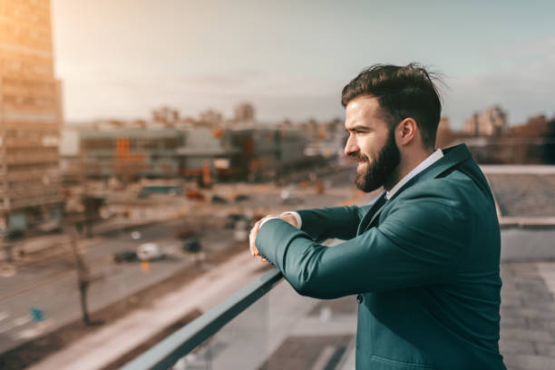 perfil del empresario barba, apoyado en la cerca y mirando a ver estando en la azotea. - men on roof fotografías e imágenes de stock