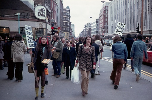 London, England, UK, 1974. Students distribute leaflets in a busy shopping street. Also: pedestrians, shops, buildings and traffic.