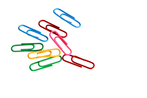Various colors paper clips lie across a white  background.
