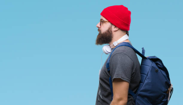 young hipster man wearing red wool cap and backpack over isolated background looking to side, relax profile pose with natural face with confident smile. - portrait human face men overweight imagens e fotografias de stock