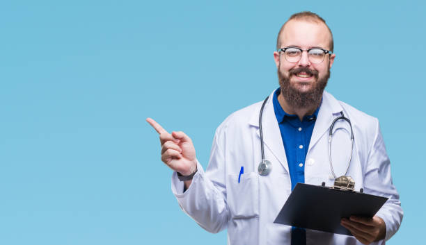 young doctor man holding clipboard over isolated background pointing and showing with thumb up to the side with happy face smiling - hand sign index finger human finger human thumb imagens e fotografias de stock