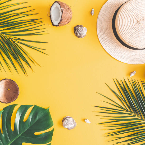istock Summer composition. Tropical palm leaves, hat, coconut on pastel yellow background. Summer concept. Flat lay, top view, copy space, square 1127774340